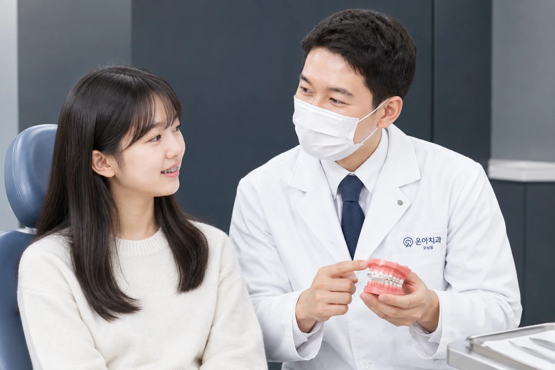 교정 장치를 부착한 환자에게 의료진이 교정 치아 모형으로 설명하는 모습 (참고 이미지)