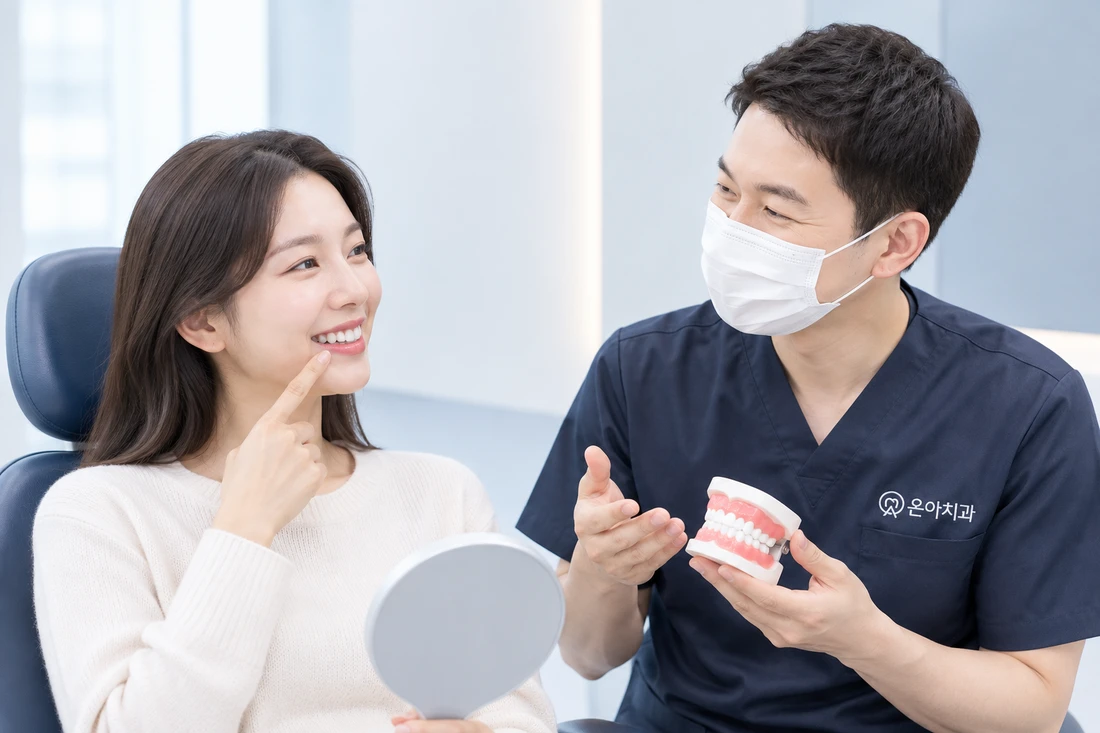 거울을 든 환자가 밝게 웃으며 앞니를 가리키고 의료진이 치아 모형으로 설명하는 모습 (참고 이미지)